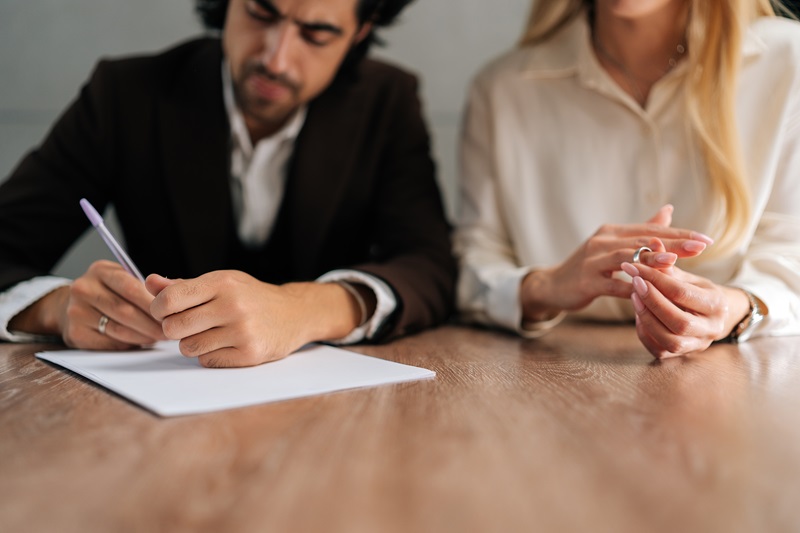 Cropped shot of spouses couple signing decree papers getting divorced in lawyers office at desk. Unhappy married family split break up end relationships giving permission to marriage dissolution.