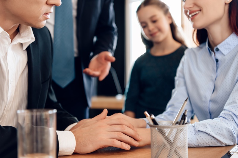 Wife and husband put their hands on each other while sitting by a lawyer in the booth. Young man and beautiful woman decide who will be main guardian of little girl.